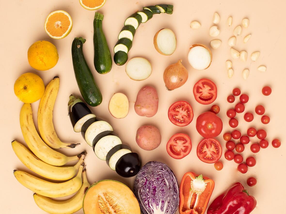 Vielfalt an Obst und Gemüse, darunter Bananen, Zucchini, Tomaten und Paprika, auf einem hellen Untergrund.